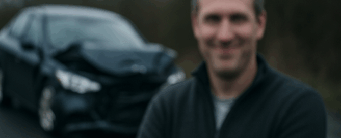 Smiling person in front of crashed car (blurred)